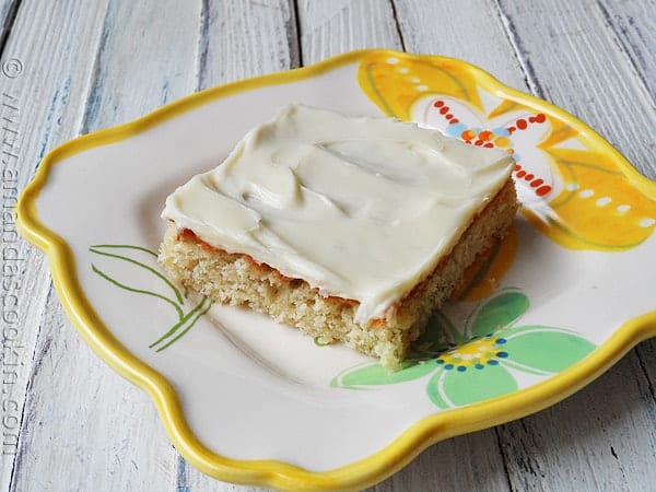 A close up photo of a banana bar with vanilla cream cheese frosting on a plate.