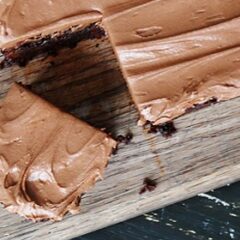 A close up photo of fudge frosted espresso brownies on a wooden cutting board.