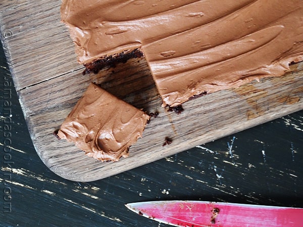 A overhead photo of pan of fudge frosted espresso brownies on a wooden cutting board.