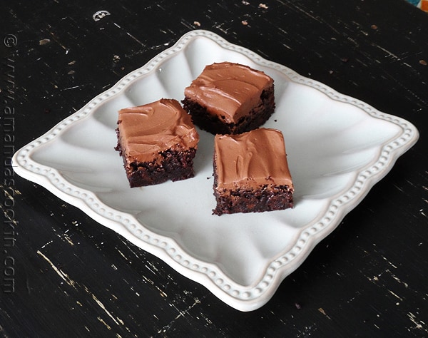 A close up photo of fudge frosted espresso brownies on a white platter.