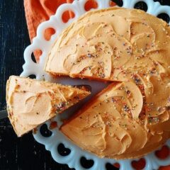 An overhead photo of an orange poke cake with a slice being removed.