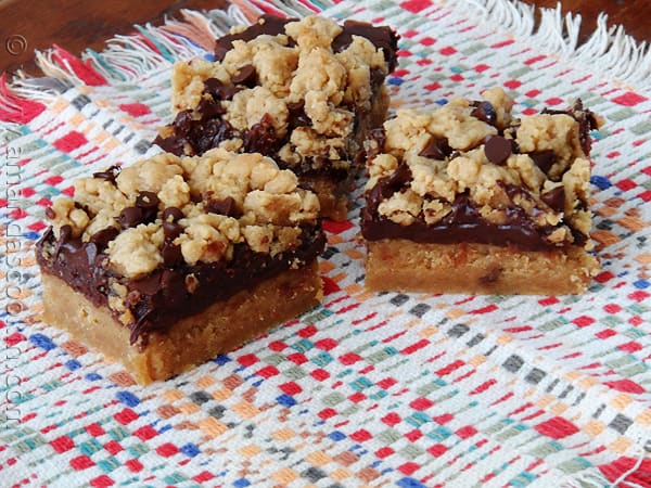 A photo of three peanut butter chocolate layer bars resting on a multicolored napkin.