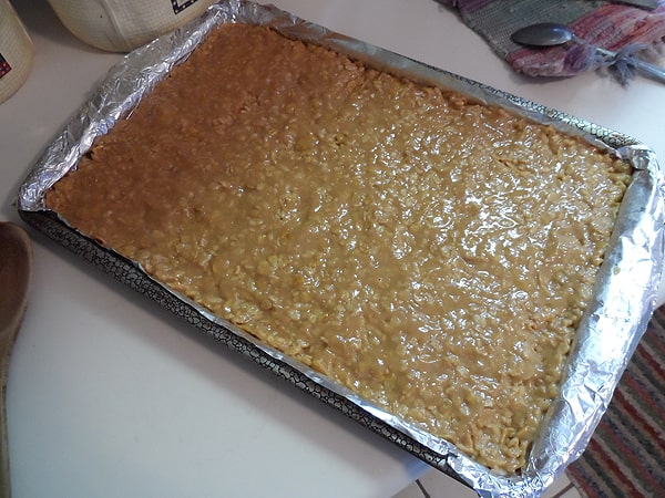 A mixture of sugar, corn syrup, peanut butter, corn and rice cereals pressed into a lined cookie sheet.