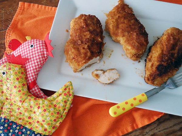 An overhead photo of three oven fried chicken breasts on a white plate.