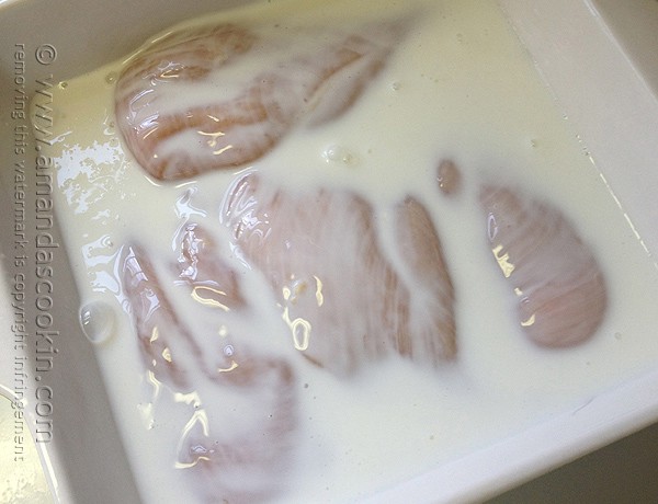 A close up photo of raw chicken breasts soaking in buttermilk.