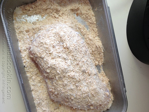 An overhead photo of a raw chicken breast in crumb coating.
