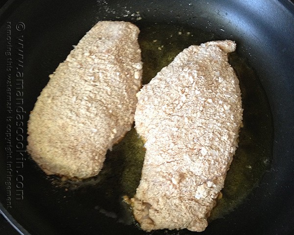 Two chicken breasts covered in crumb coating in a skillet.