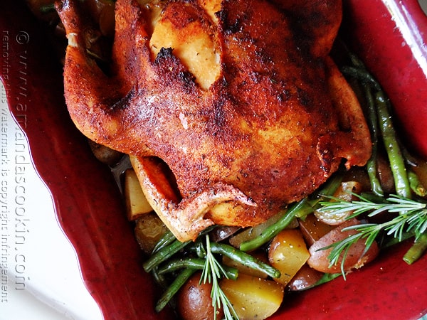 A close up photo of a whole roasted chicken over vegetables in a roasting pan.