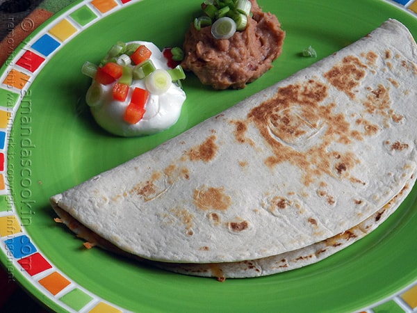 An overhead photo of a beef and bean quesadilla on a green plate with sour cream and refried beans on the side.