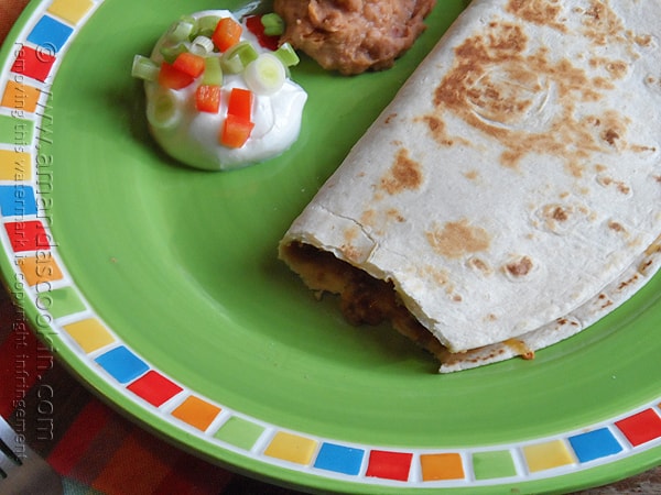 A close up photo of a beef and bean quesadilla on a green plate with sour cream and refried beans on the side.