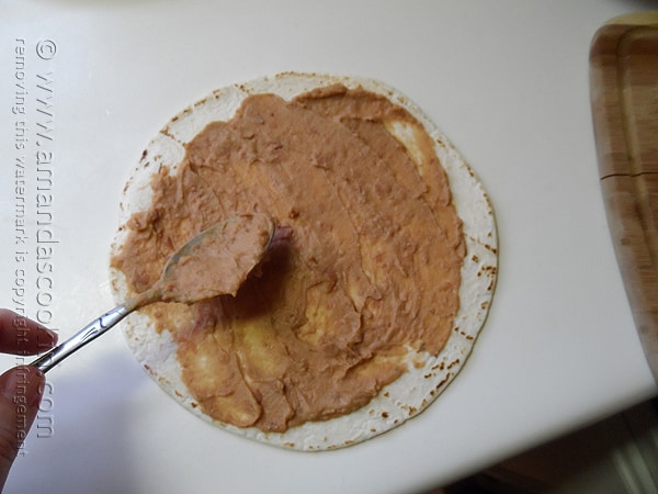 An overhead photo of a tortilla with refried beans spread on top.