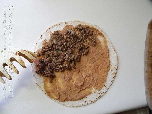 An overhead photo of a tortilla with refried beans and ground beef on top. 