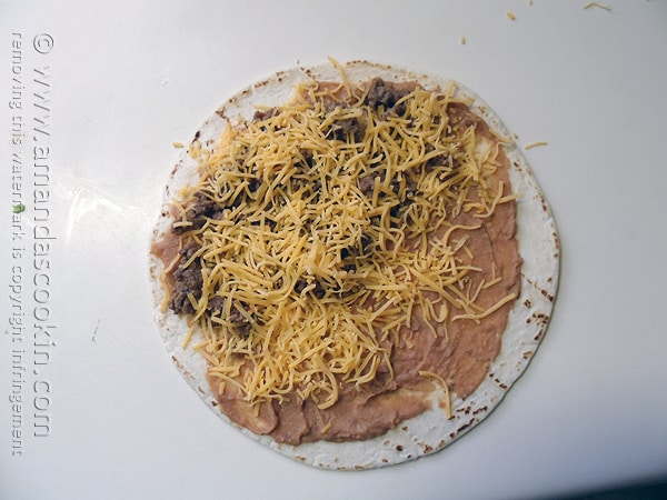An overhead photo of a tortilla with refried beans, ground beef and shredded cheese on top. 