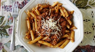 An overhead photo of penne Bolognese with grated parmesan cheese on top.