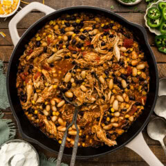 Skillet of shredded chicken chili with black beans, white beans and corn with a serving spoon