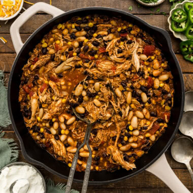 Skillet of shredded chicken chili with black beans, white beans and corn with a serving spoon