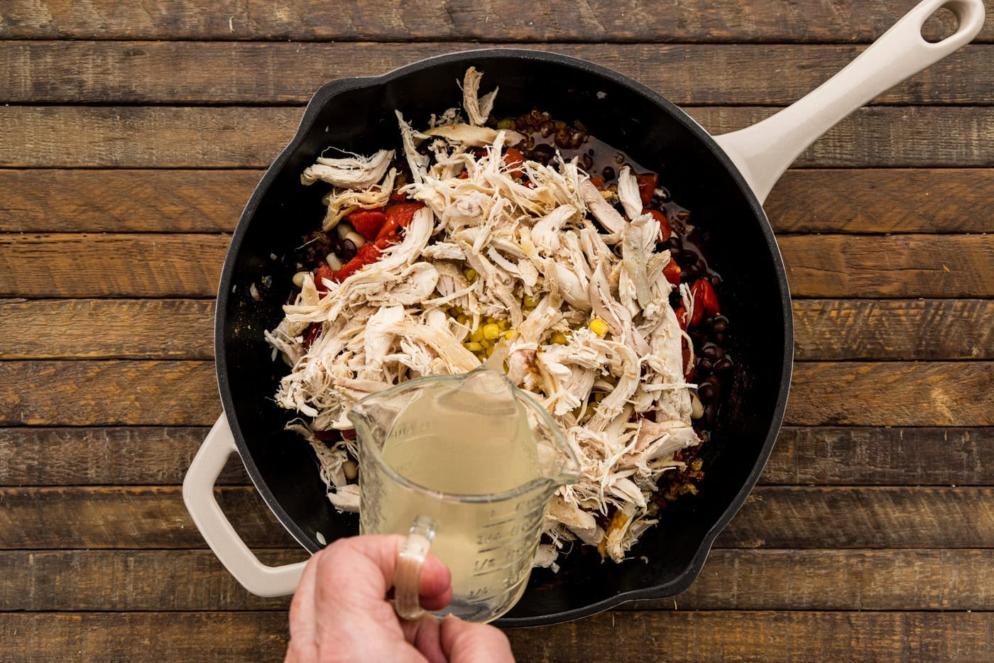 Chicken broth being poured over shredded rotisserie chicken in the skillet