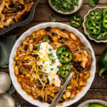 Bowl of black bean chicken chili topped with sour cream, shredded cheese, jalapeño slices and cilantro with lime wedges on the side