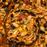 Close up of a ladle lifting shredded chicken, black beans, white beans and corn out of a pot of chili