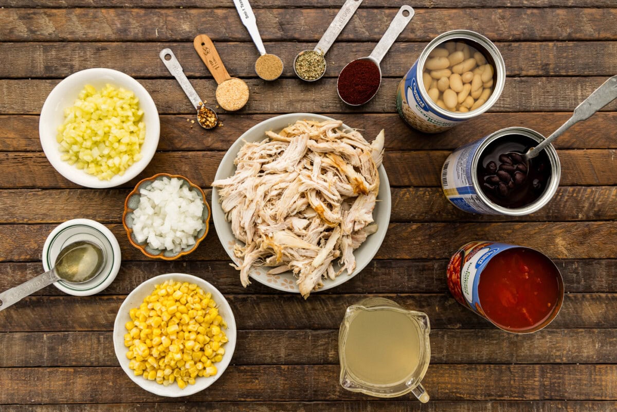 Ingredients for chicken chili with black beans and corn including shredded rotisserie chicken, banana peppers, onion, spices, canned beans, diced tomatoes, frozen corn and chicken broth