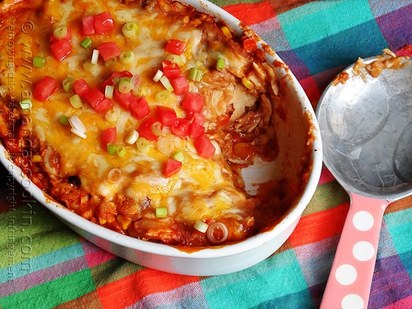 An overhead photo of a chicken tostada casserole with chopped green onions and tomatoes on top with a serving missing.