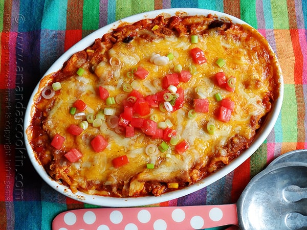 An overhead photo of a chicken tostada casserole with chopped green onions and tomatoes on top.