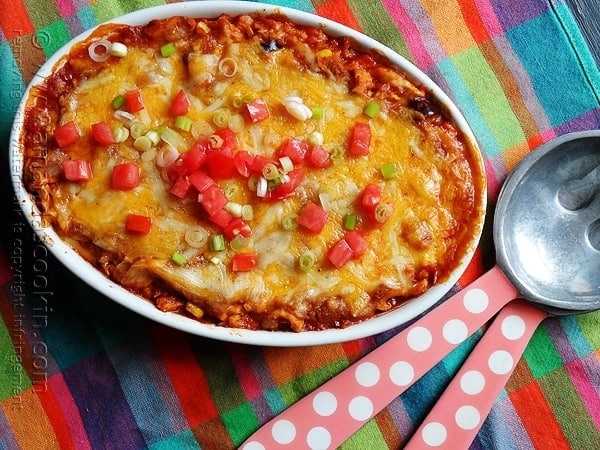 An overhead photo of a chicken tostada casserole with chopped green onions and tomatoes on top.