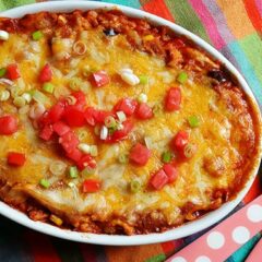 An overhead photo of a chicken tostada casserole with chopped green onions and tomatoes on top.