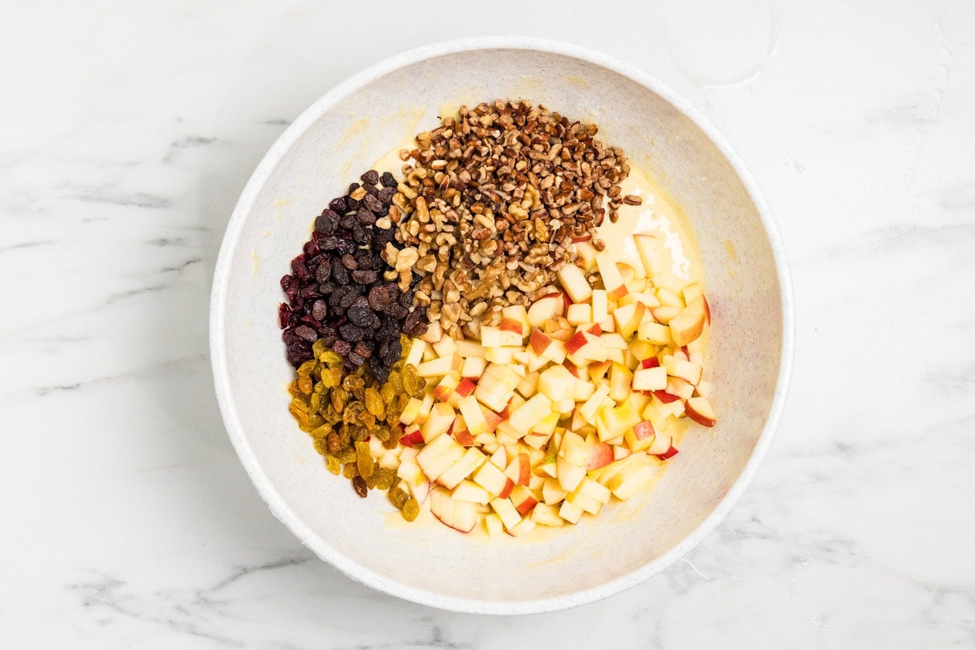 cake batter in bowl with fresh apples, raisins, nuts and craisins