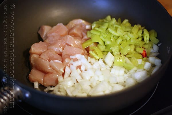 A close up photo of cubed chicken, banana peppers and onions in a skillet.