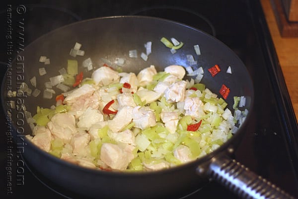 A close up photo of cubed chicken, banana peppers and onions cooking in a skillet.