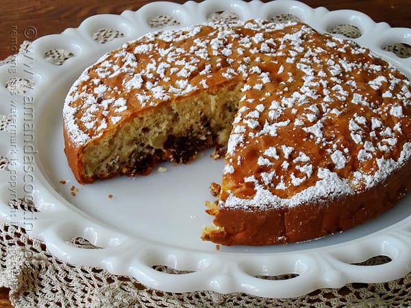 A close up photo of a Merryfield apple cake on a decorative white platter with a slice missing. 