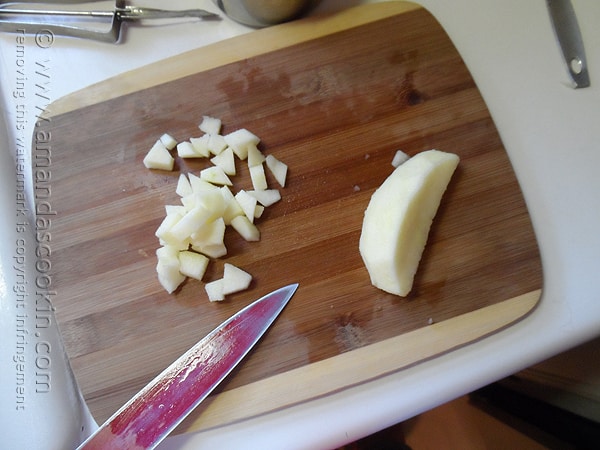 An overhead photo of an apple being chopped up on a wooden cutting board.