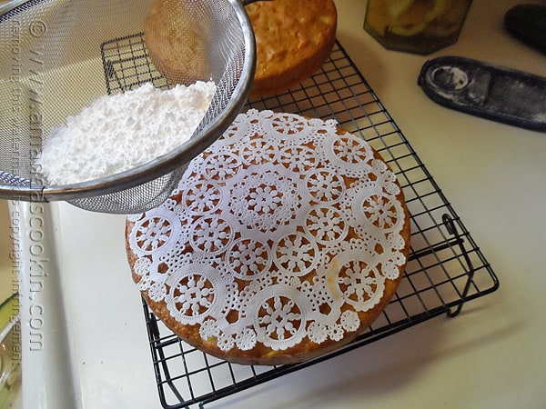 A photo of powdered sugar being sprinkled over a Merryfield apple cake on a cooling rack.