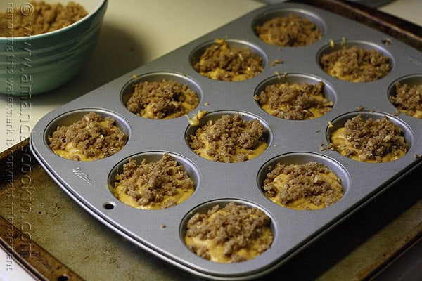 A close up photo of a muffin tin filled with pumpkin mini cake batter and cinnamon streusel topping.