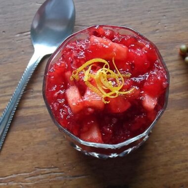 A close up photo of cranberry relish in a glass bowl with a spoon laying next to it.