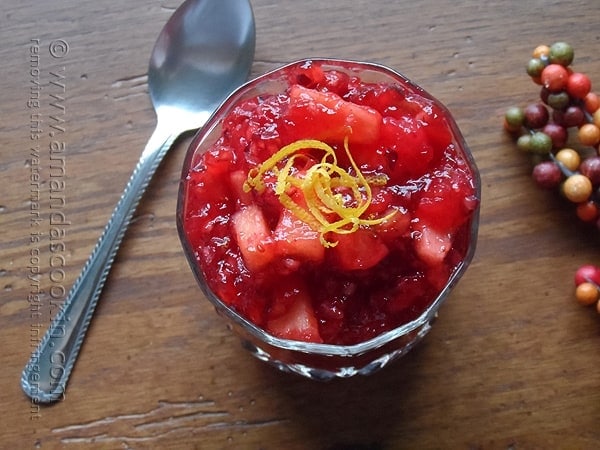 A close up photo of cranberry relish in a glass bowl with a spoon laying next to it.