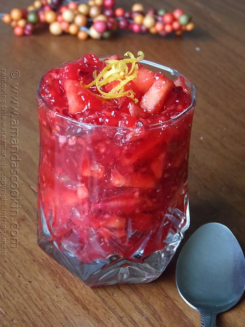 A close up photo of cranberry relish in a glass bowl with a spoon laying next to it.