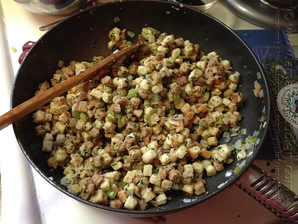 A close up photo of cubed stuffing with chopped onions and celery in a skillet.