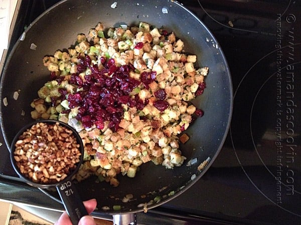 A photo of dried cranberries and pecans being added to the skillet of stuffing.