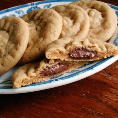 A close up of a Hershey drop stuffed peanut butter cookie split in half on a plate with whole cookies in the background.