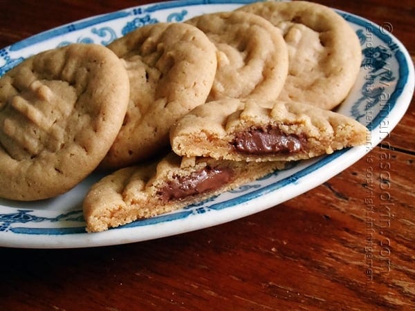 A close up of a Hershey drop stuffed peanut butter cookie split in half on a plate with whole cookies in the background.