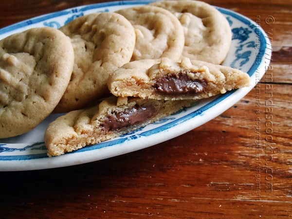 A close up of a Hershey drop stuffed peanut butter cookie split in half on a plate with whole cookies in the background.