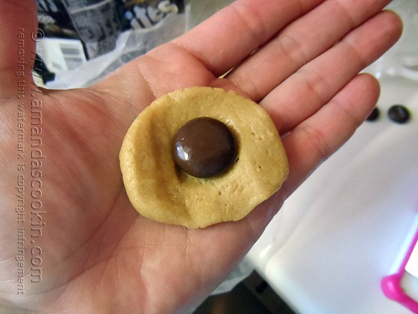 A photo of a hand holding flattened cookie dough with a Hershey drop on top.