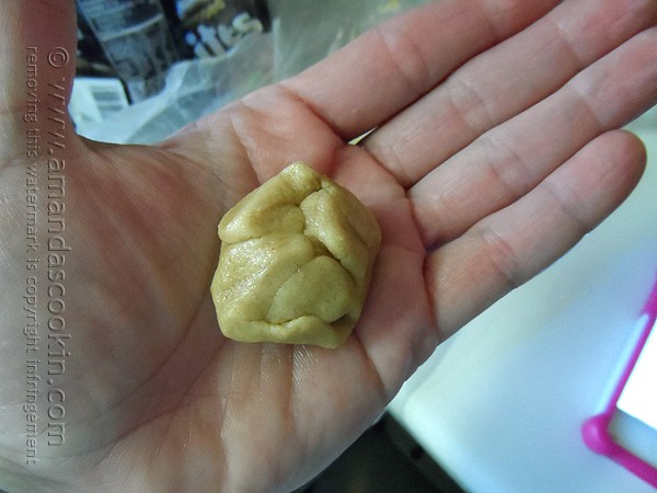 A photo of a hand holding rolled up cookie dough with a Hershey drop inside.