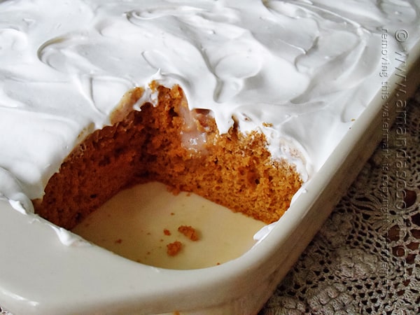 A close up photo of a pumpkin pudding poke cake in a baking dish with a square missing.