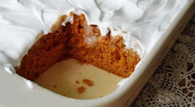 A close up photo of a pumpkin pudding poke cake in a baking dish with a square missing.