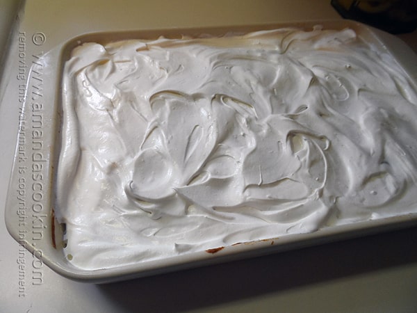 A photo of whipped topping spread over a pumpkin pudding poke cake.
