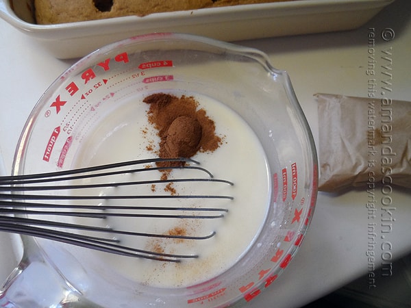 A close up photo of pudding mix, cinnamon and milk in a large measuring cup with a whisk.