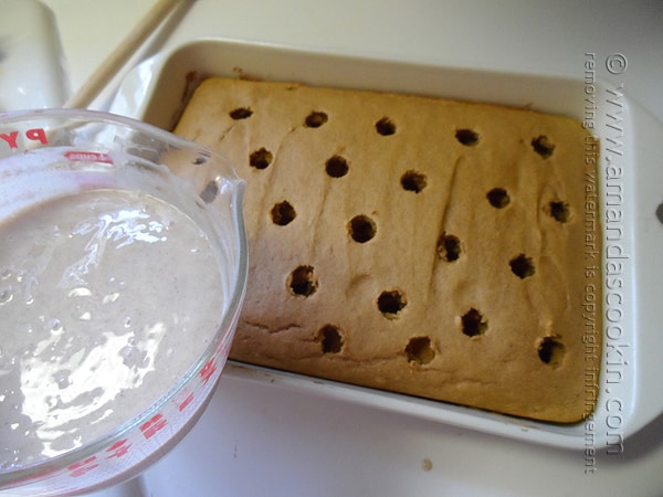 An overhead photo of pumpkin cake in a baking dish with holes and a measuring cup of pudding about to be poured onto the cake.
